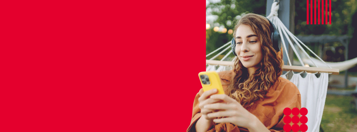 Sieviete ar austiņām ārā guļ šūpuļtīklā un skatās telefonā. 