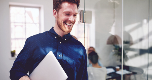 Мужчина с ноутбуком стоит у стеклянных офисных дверей.