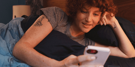 Девочка удобно лежит в кровати и смотрит в телефон. at her phone. 